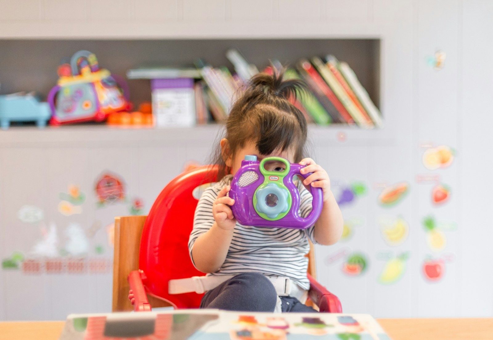 petite enfance girl holding purple and green camera toy