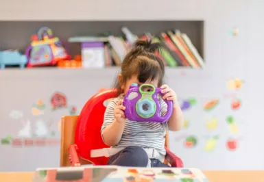 petite enfance girl holding purple and green camera toy