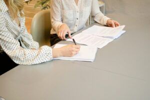 conciliateur de justice woman signing on white printer paper beside woman about to touch the documents