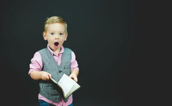 Raconte-moi une histoire boy wearing gray vest and pink dress shirt holding book