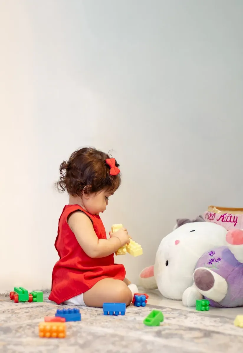 a little girl in a red dress playing with a stuffed animal