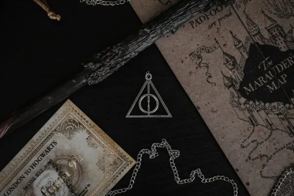harry potter A metal Deathly Hallows pendant, a wand, and a map on a black surface