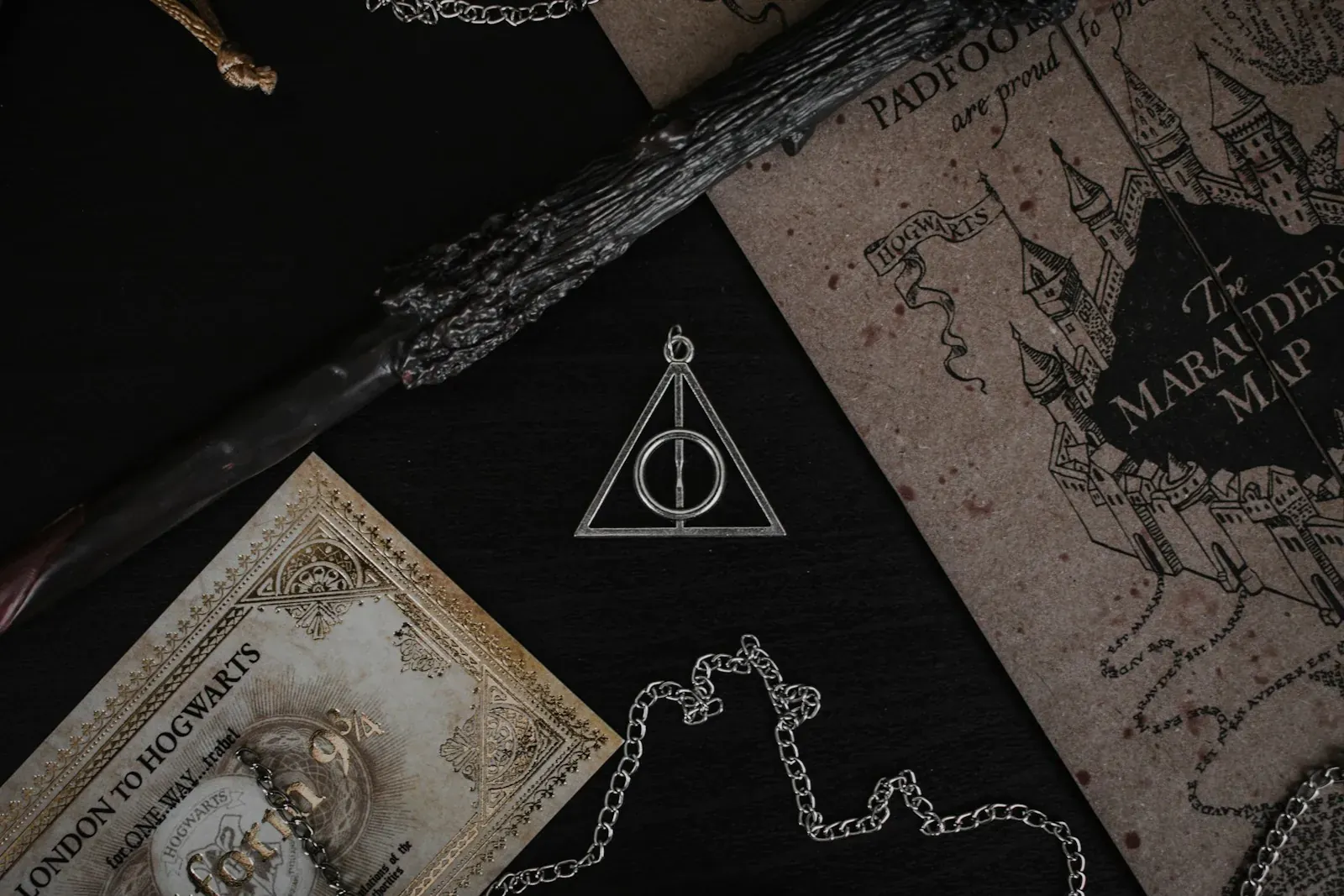 harry potter A metal Deathly Hallows pendant, a wand, and a map on a black surface